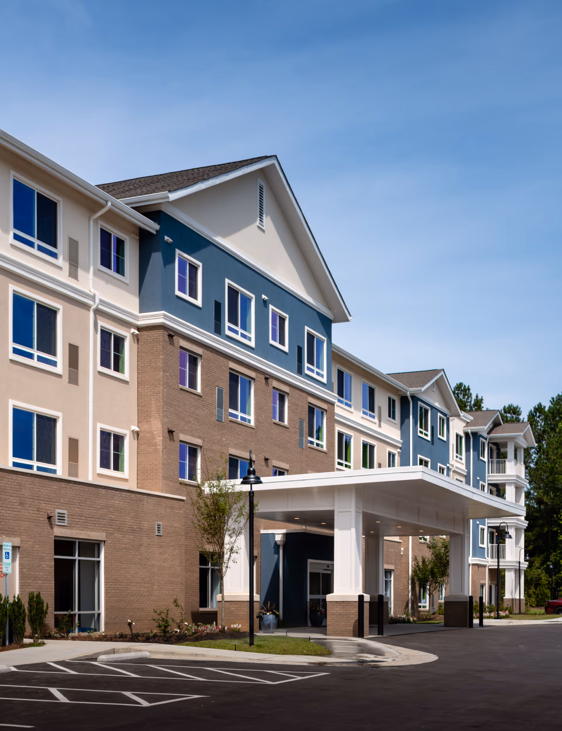 Front entrance of a multi-story senior living building with a covered porte-cochère, blue and beige facade and windows.