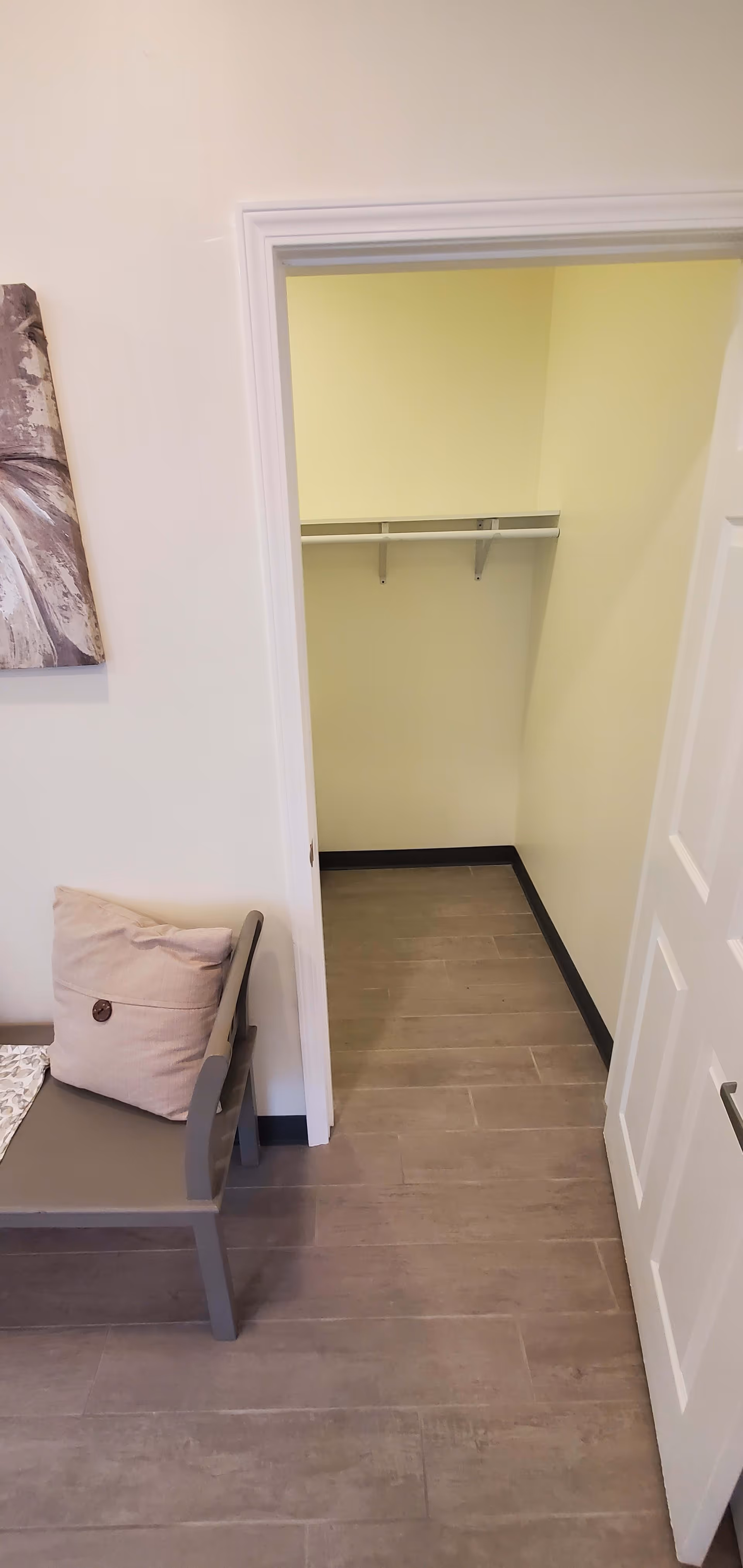 Open doorway showing a small empty closet with a shelf and a bench with a cushion in the foreground.