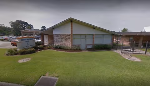 Front exterior view of Gonzales Healthcare Center with a manicured lawn and a gated entrance.