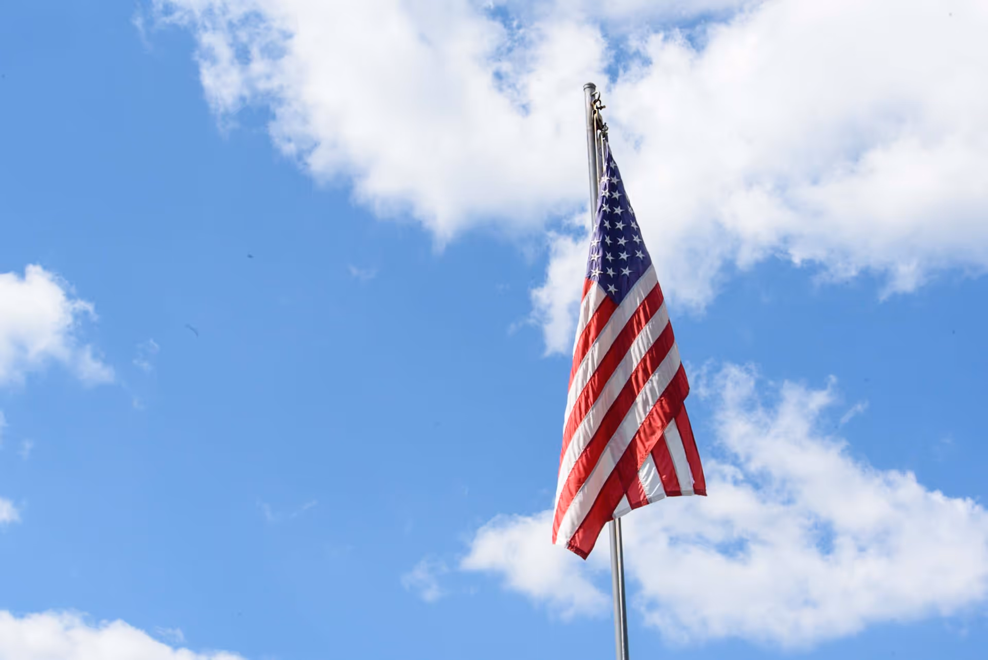 An American flag flying on a flagpole against a blue sky with scattered white clouds.