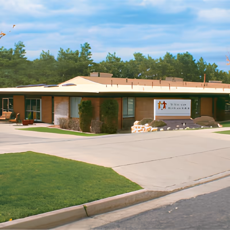 Single-story building front with a driveway, lawn and an entrance sign at a senior care facility.