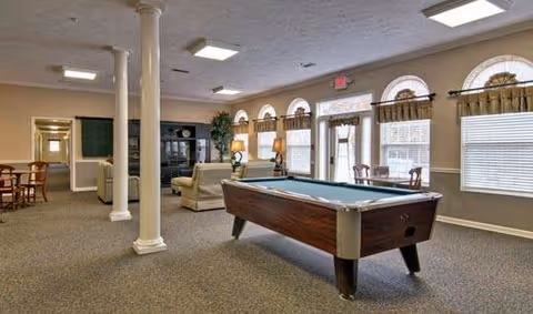 Spacious senior living common room with a pool table, seating area, columns, and arched windows along one wall.