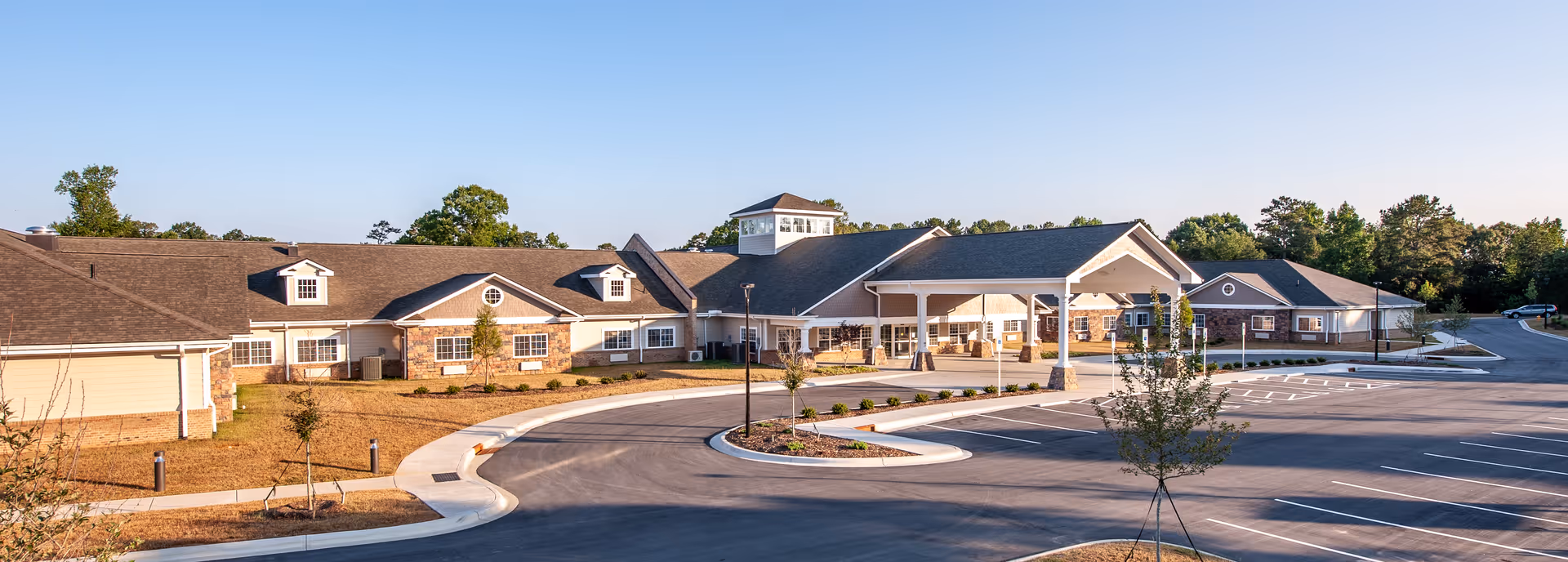 Front exterior of Grace Village Assisted Living and Memory Care showing a single-story brick and siding building with a covered entry, circular driveway, and empty parking lot.
