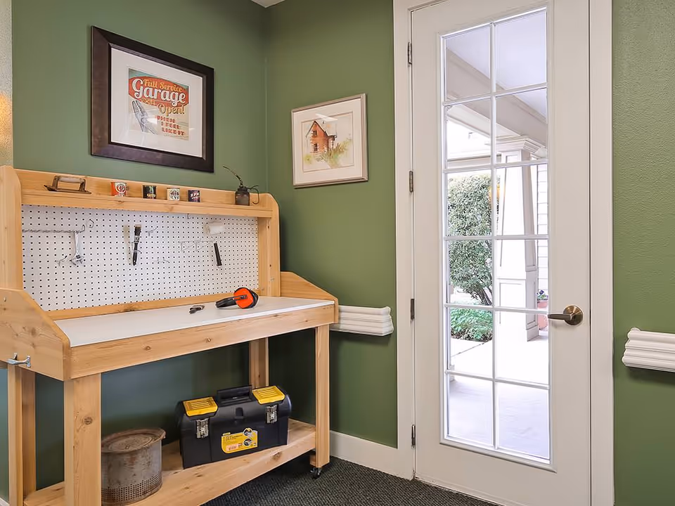 Small indoor workshop area with a wooden workbench and pegboard against a green wall next to a glass-paneled door.