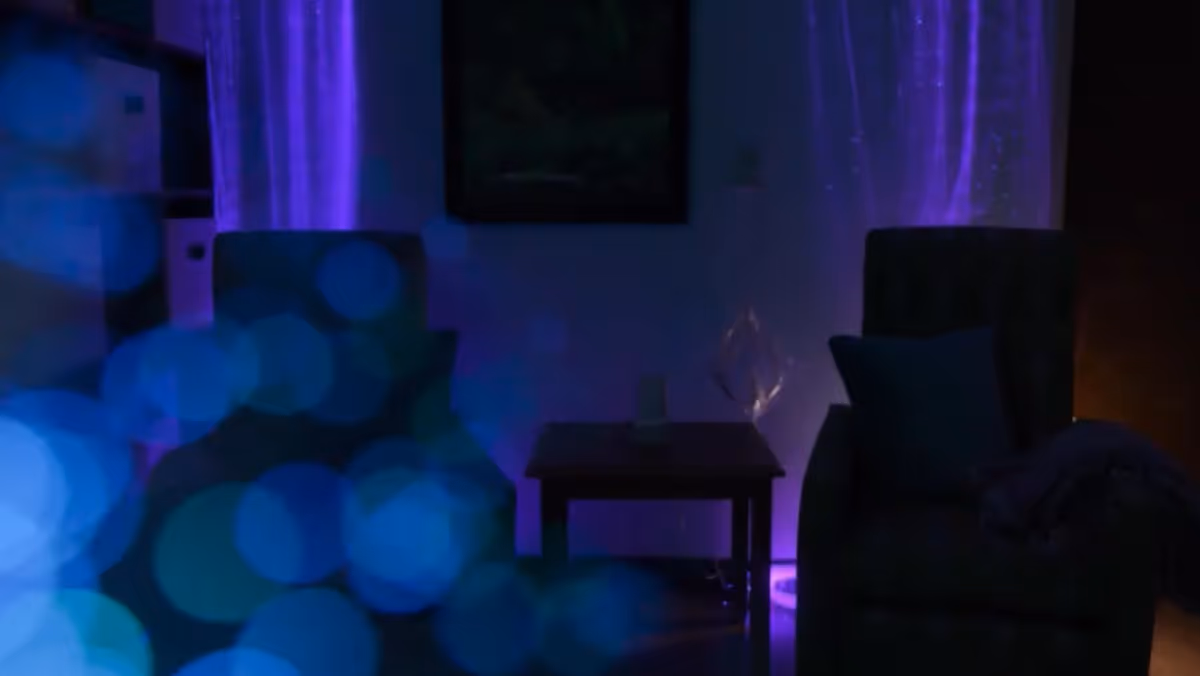 Dimly lit room with two armchairs separated by a small wooden table. Purple lighting illuminates the curtains behind the chairs, creating a calm and cozy atmosphere.