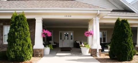Front entrance of a brick building with white columns, planters, and pink hanging baskets.