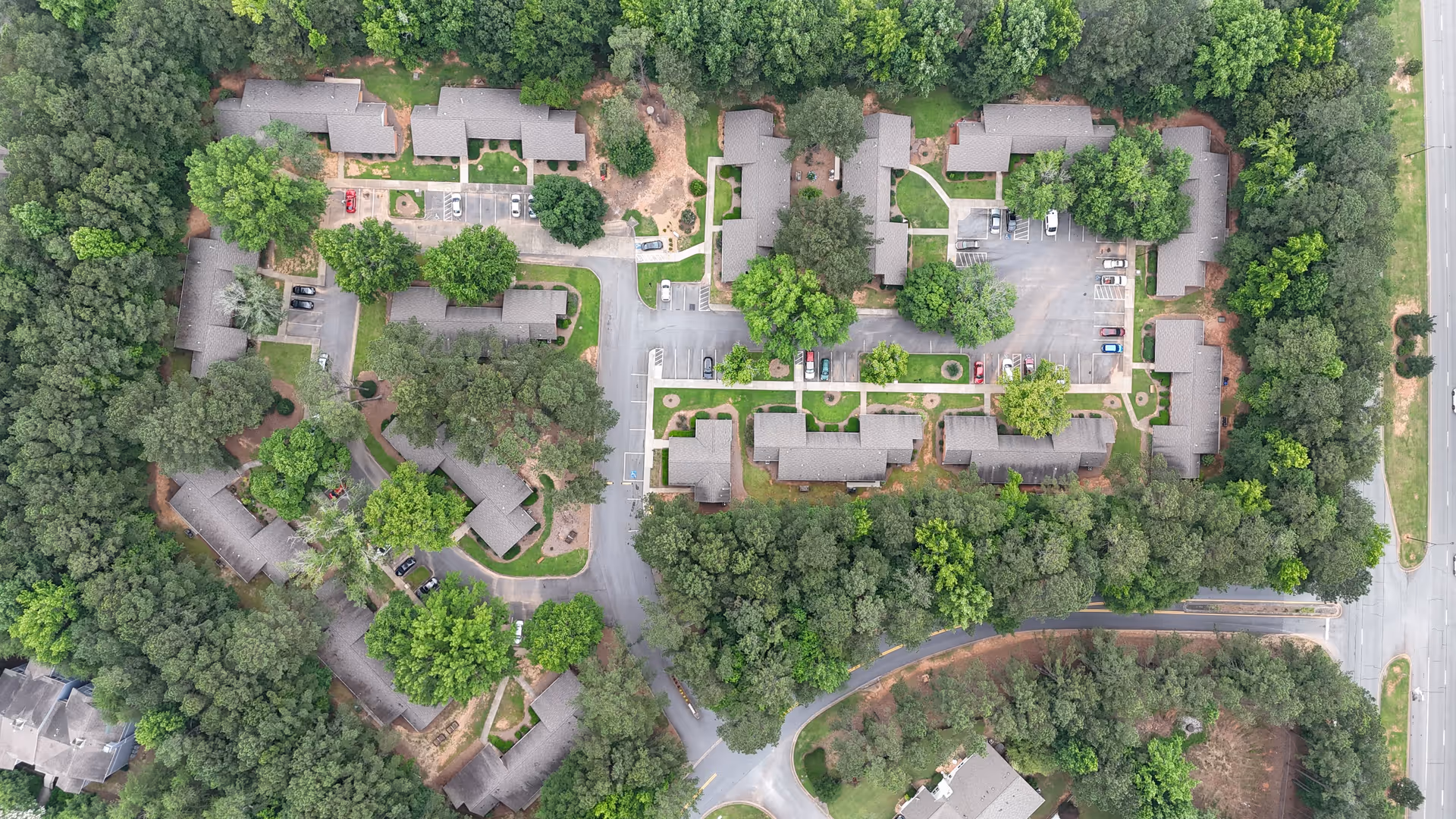 Aerial view of Shenandoah Villas senior living facility showing multiple buildings surrounded by dense trees, parking lots with cars, and paved roads.