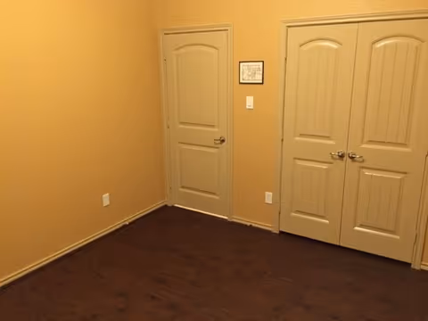A small interior hallway with tan walls, dark wood floor, and multiple white doors.