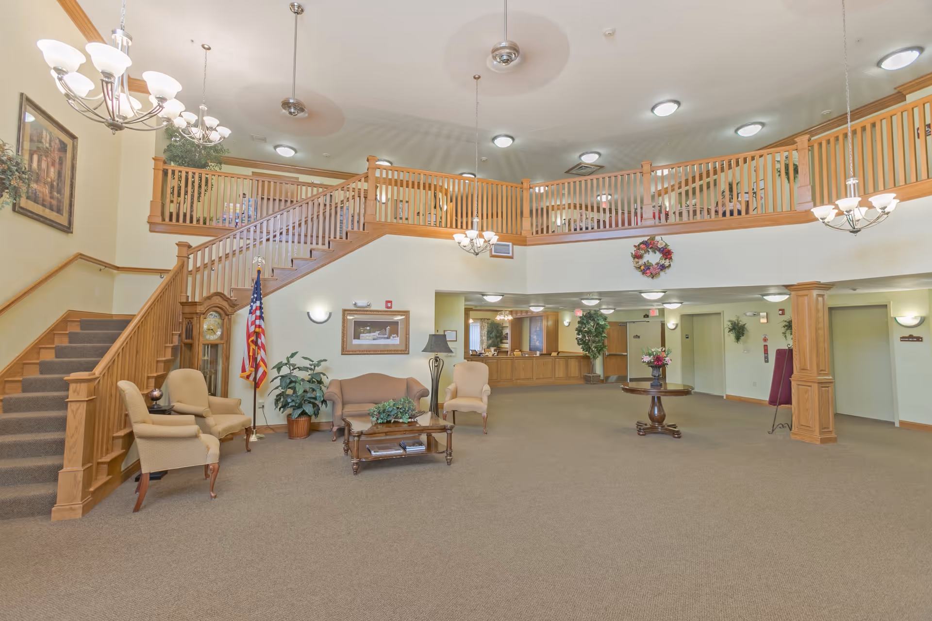 Spacious two-story lobby with seating area, wooden staircase, reception desk, and chandeliers.