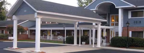 Exterior view of Plantation Oaks Senior Living Residence entrance with a covered porte-cochere and white columns.