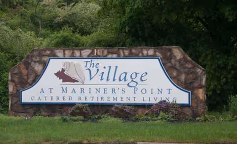Entrance sign for The Village at Mariner's Point surrounded by greenery and stone.