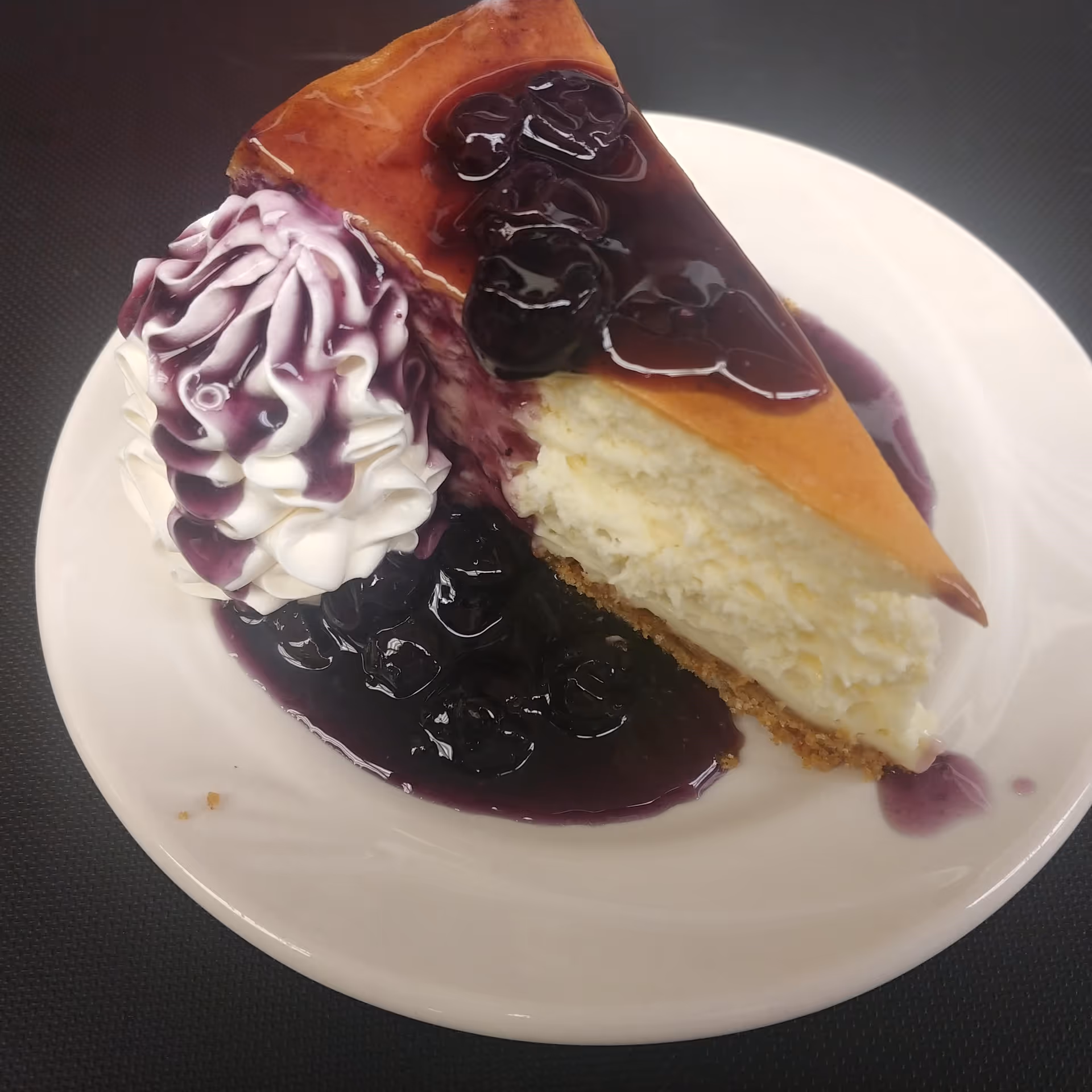 A slice of cheesecake topped with blueberry compote and a dollop of whipped cream on a white plate.