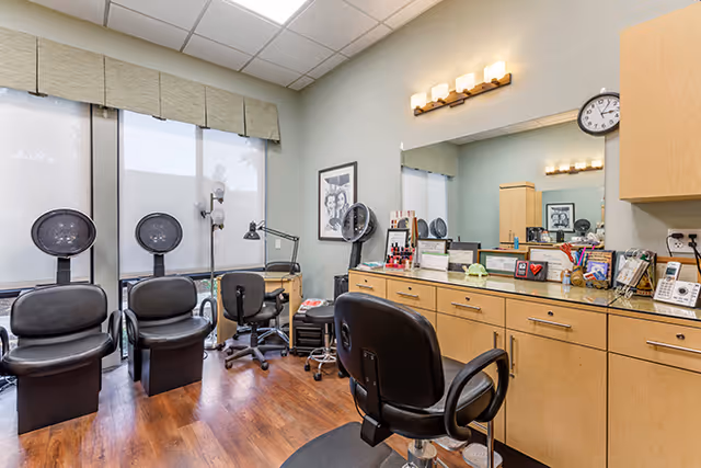 A bright salon room with styling chairs, hooded hair dryers, a large mirror, and a counter stocked with hair-care products.