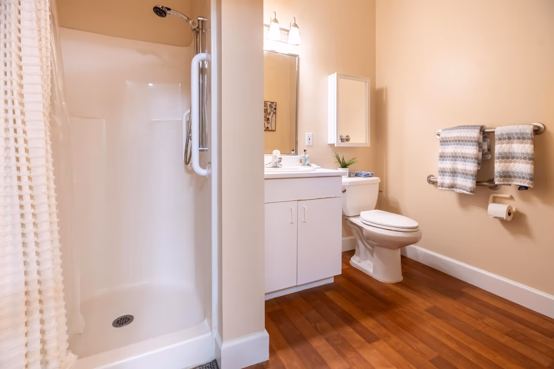 Bathroom with a corner shower, white vanity and toilet, and towels hanging on a wall-mounted bar.