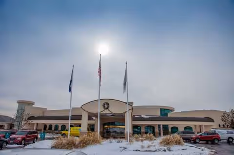 Snowy exterior view of Delmar Gardens of O'Fallon entrance with flags and parked cars.
