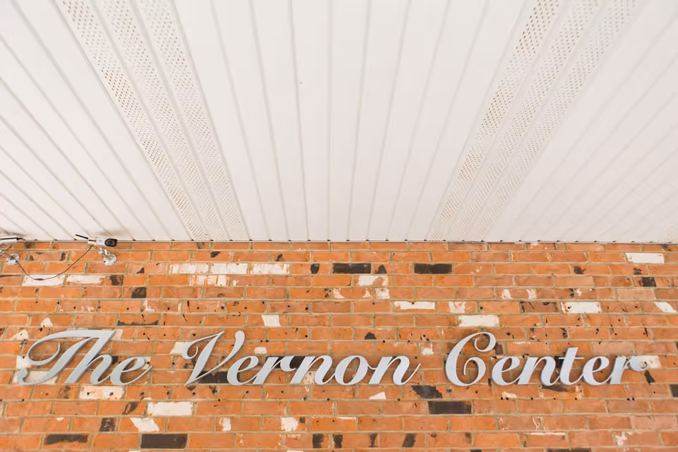 Brick wall with a metal script sign reading 'The Vernon Center' beneath a white paneled overhang.