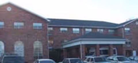 Red brick senior living facility with covered entrance and parked cars in front.