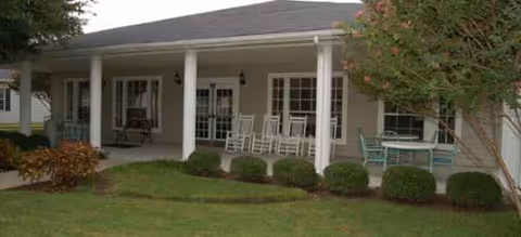 Covered front porch with white columns, rocking chairs, and shrubs at Brookdale Tanglewood Oaks.