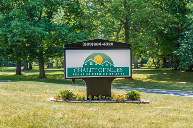A freestanding sign on a grassy lawn reading 'Chalet of Niles Nursing and Rehabilitation Center' with a phone number, set against a backdrop of trees.