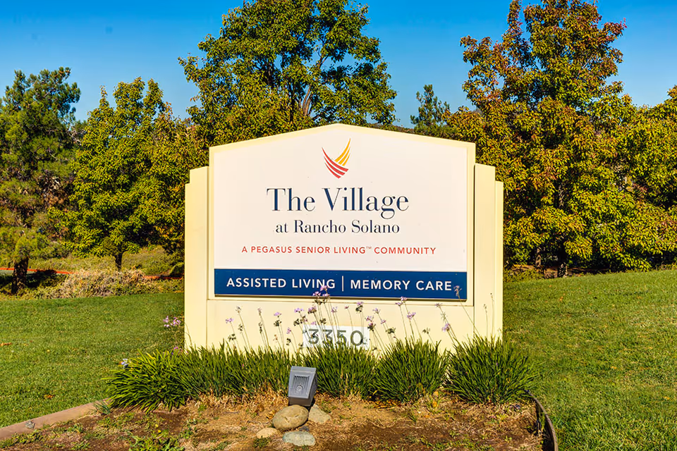 A freestanding entrance sign reading "The Village at Rancho Solano" on a grassy lawn with trees in the background.