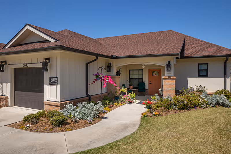 Front exterior of a single-story home with a garage, landscaped walkway, and a covered porch with potted plants.