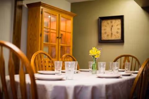 Round dining table set with white tablecloth, glassware, plates, and a yellow flower centerpiece.