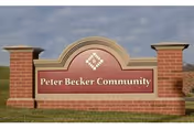A brick and stone sign for Peter Becker Community set on a grassy area with a cloudy sky in the background.