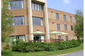 Three-story brick medical facility building with a ground-level patio, umbrellas, and landscaped shrubs in front.