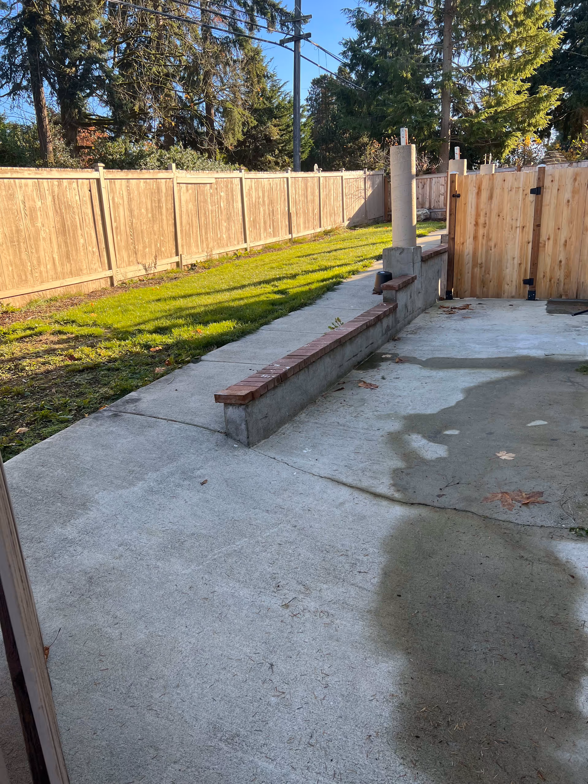 Concrete patio and walkway leading to a grassy fenced backyard with trees.