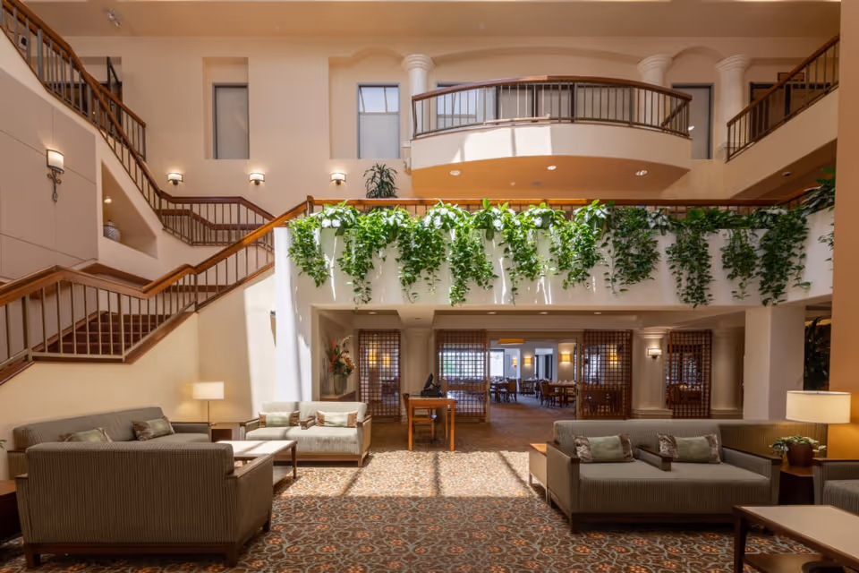 Spacious two-story atrium lounge with sofas, staircases, hanging plants, and an upper balcony.