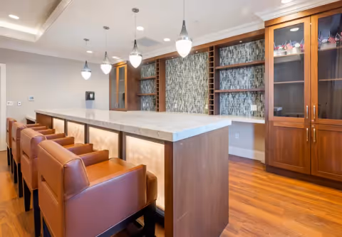 Communal dining/bar area with a marble-topped island, leather bar stools, pendant lights, and built-in wooden cabinetry.