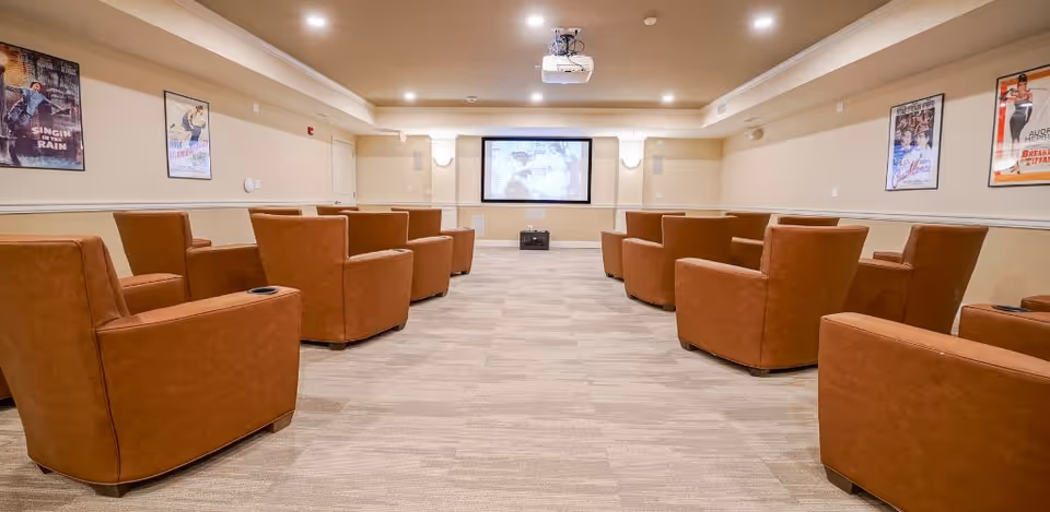 A screening room with rows of brown recliner chairs facing a projector screen and movie posters on the walls.