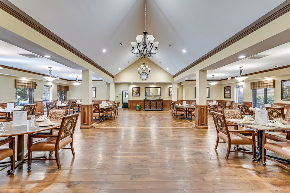 Spacious dining room with multiple set tables, chandeliers, a vaulted ceiling, and hardwood floors.