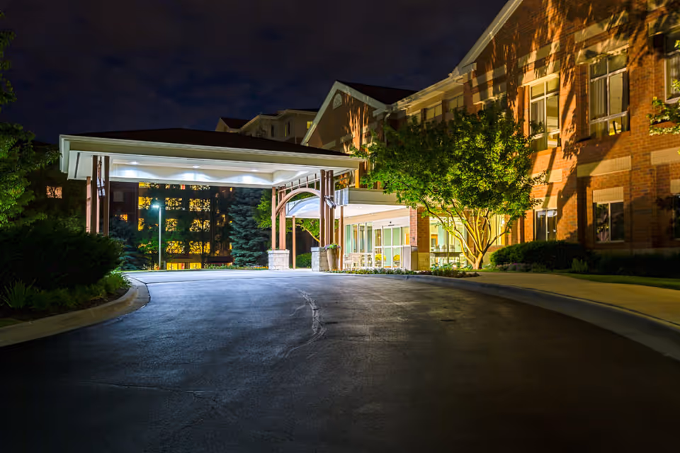 Illuminated entrance and covered drop-off canopy of a brick senior living facility at night.
