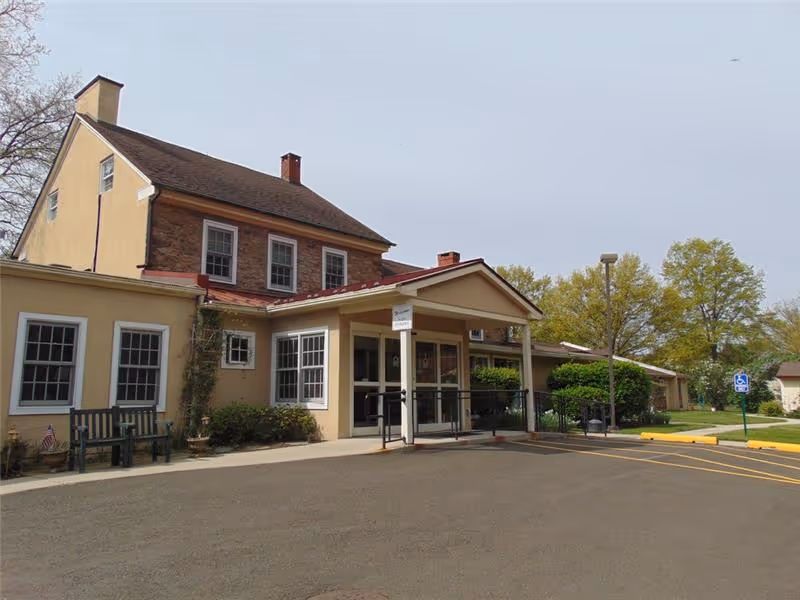 Front entrance of a two-story building with a covered portico, wheelchair ramp, benches and adjacent parking area.