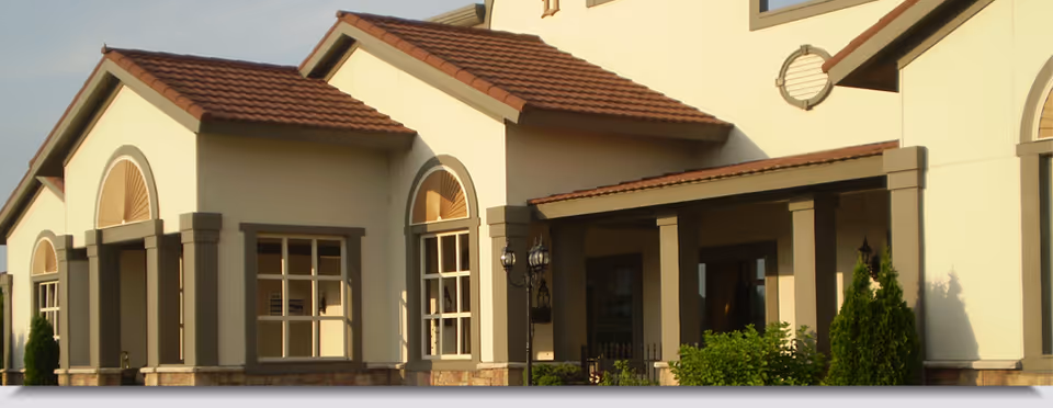 Exterior front of a building featuring arched windows, columns, a covered porch, and a red-tiled roof.