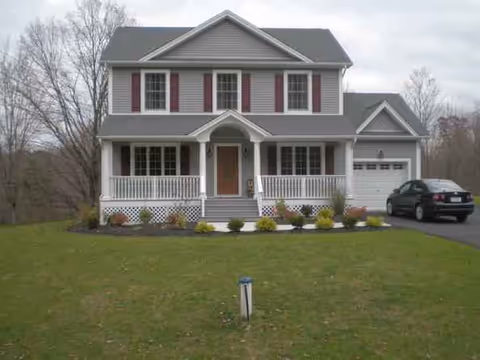 Two-story gray suburban house with front porch and manicured lawn.