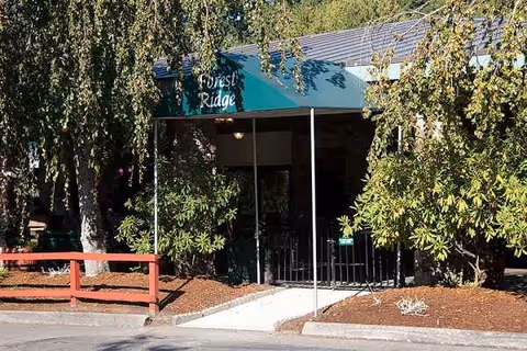 Front entrance of Forest Ridge Health & Rehab with a green canopy and trees.