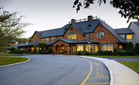 Brick senior living facility with curved road and landscaped entrance at dusk.