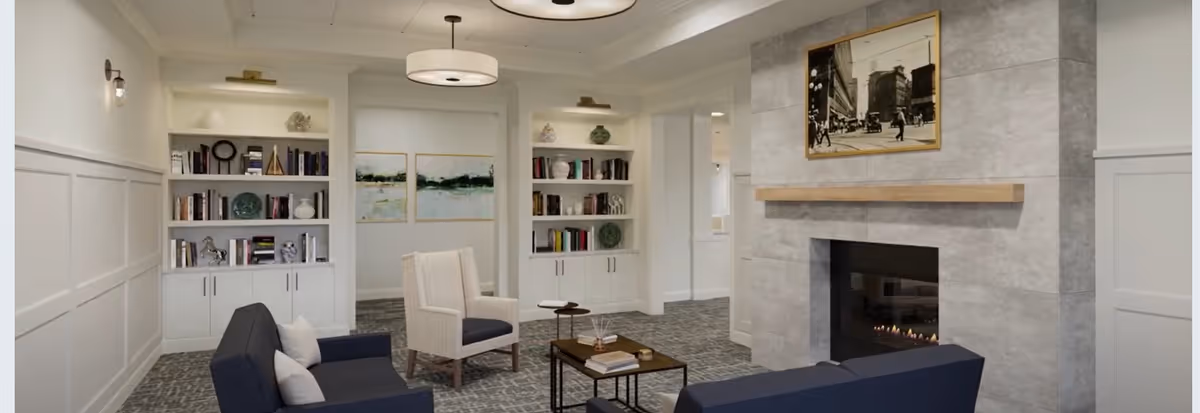 Cozy sitting area with navy sofas and armchairs arranged around a coffee table and fireplace, flanked by built-in bookshelves.