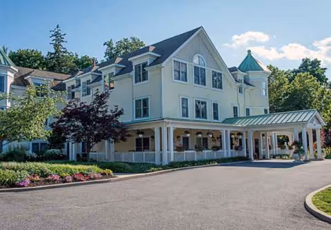 Light-colored senior living building with a covered entrance and landscaped front yard.