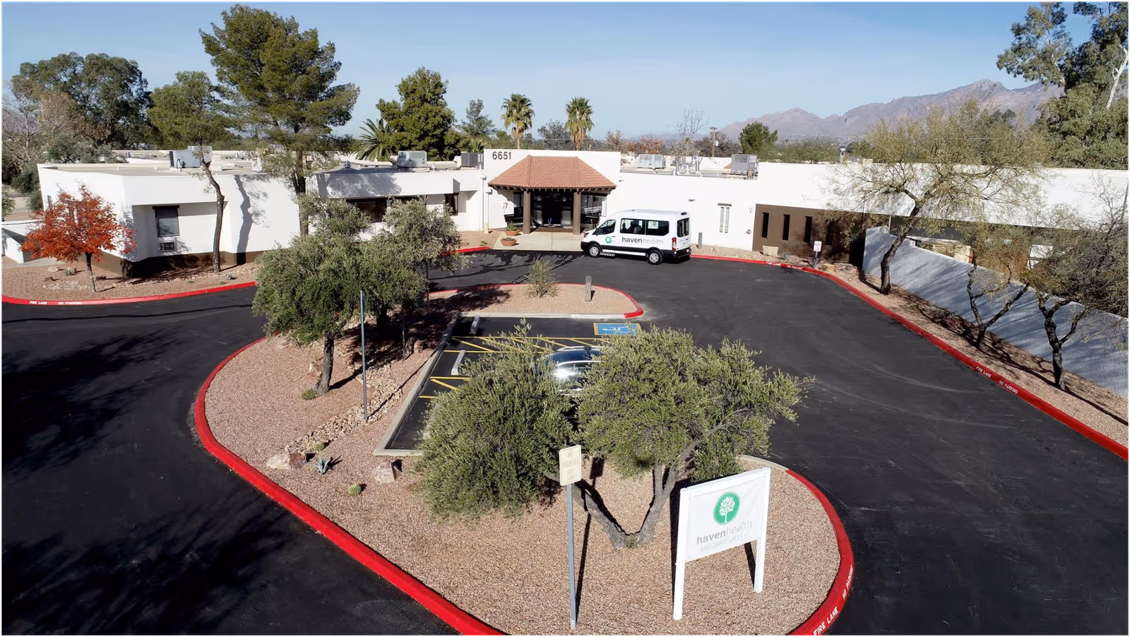 Aerial view of Haven Health Saguaro Valley's single-story building with a circular driveway, parking spaces, a shuttle van, and a front sign.