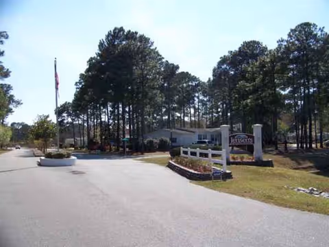 Front entrance of Ocean Pines and Magnolia Grove with sign, driveway, and tall trees.