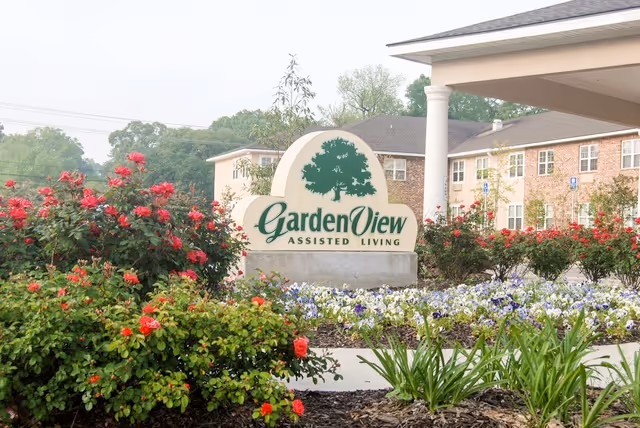 Garden View Assisted Living sign at the entrance with colorful flowering shrubs.