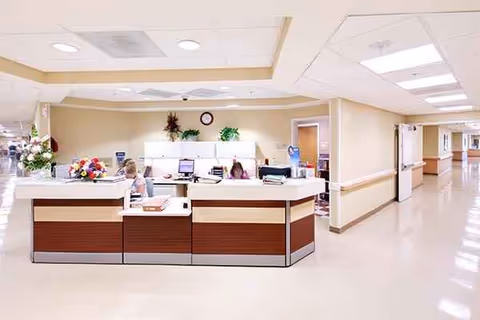 Reception desk at a senior living facility with computers, flowers, and staff behind the counter.