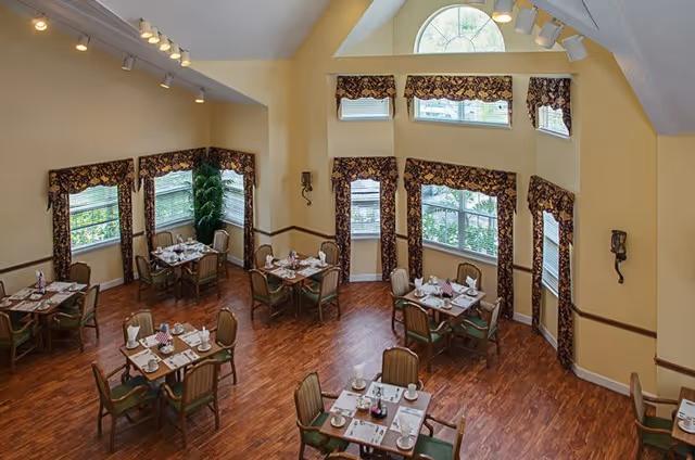 An overhead view of a dining room with tables set for meals, featuring large windows with decorative curtains and wooden flooring.