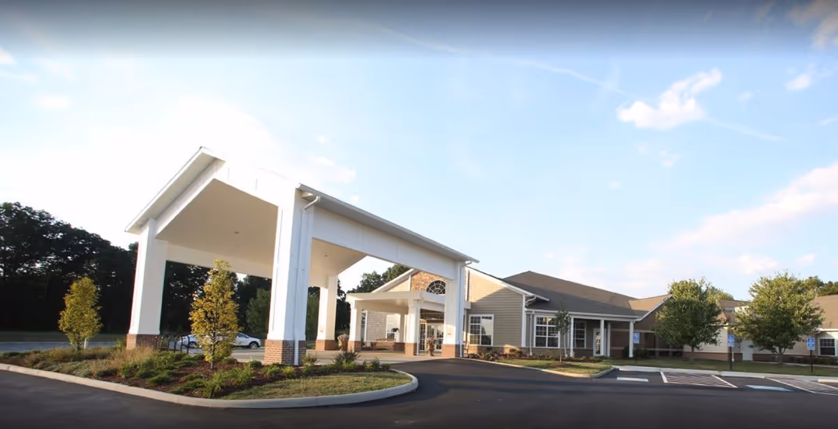 Exterior view of Danbury Massillon facility showing the main entrance with a large covered drop-off area, surrounded by landscaped greenery and a parking lot under a partly cloudy sky.