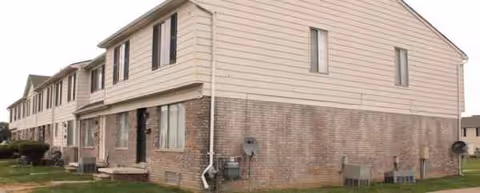 Two-story townhouse building with brick lower level, beige siding, and multiple windows.
