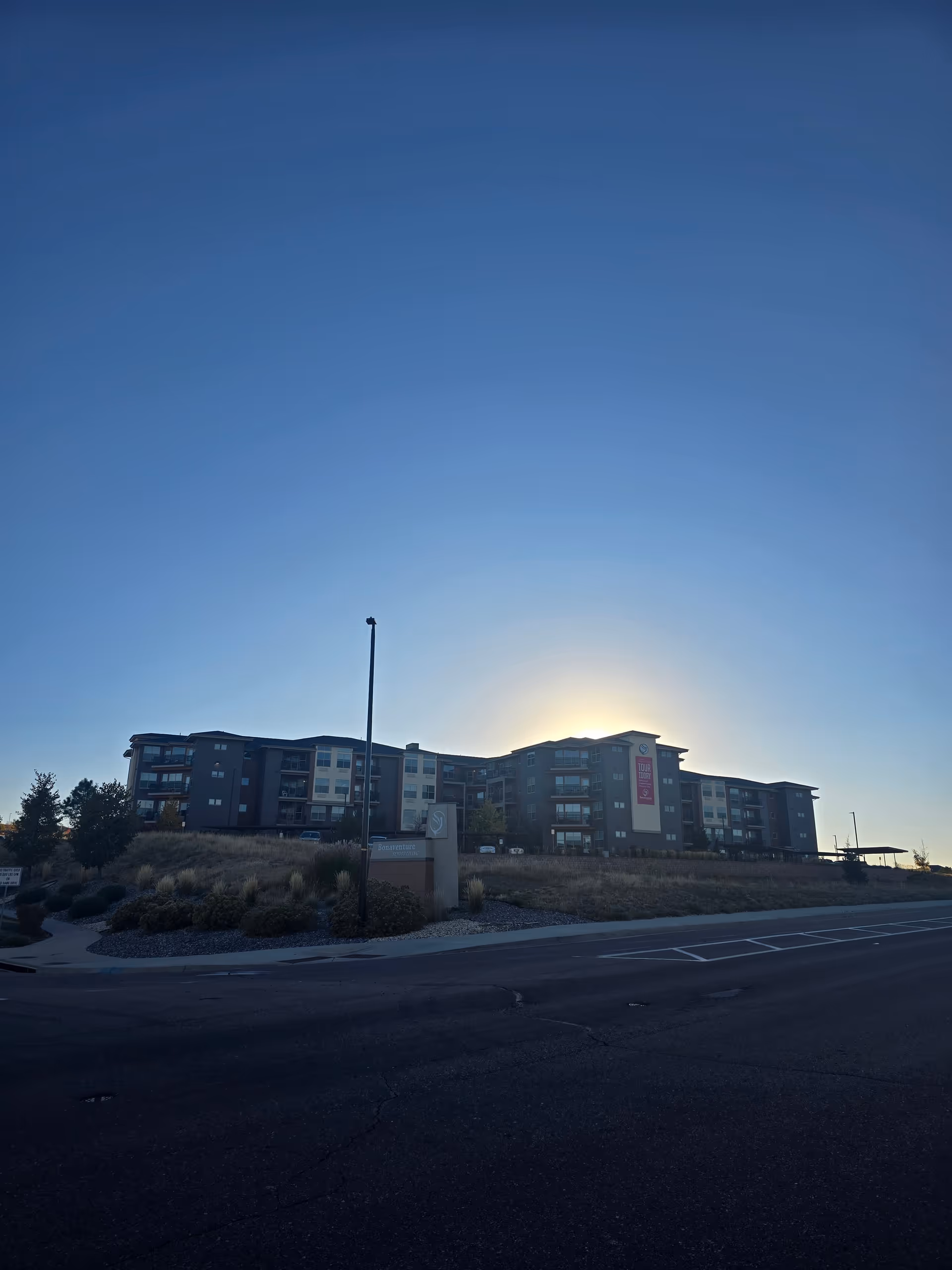 Exterior view of a multi-story senior living facility building named Bonaventure of Castle Rock during sunset with clear sky and landscaped surroundings.