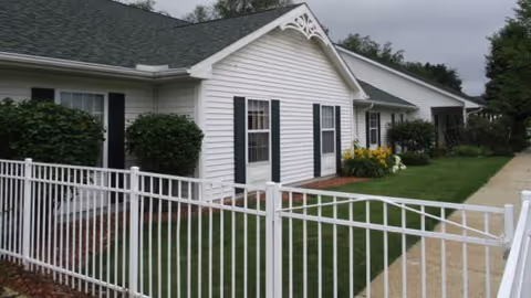 Exterior view of a white senior living building with black shutters and a white fence.